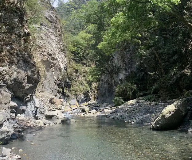narrow riverbed surrounded by mountain slope and trees